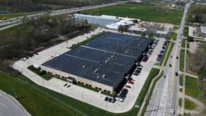 High aerial perspective looking down the length of the Jenne Distributors facility, capturing the 877 kW (DC) rooftop solar installation adjacent to the highway.