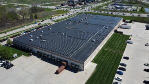 Three-quarter aerial view of the Jenne facility from the loading dock side, showing the sprawling rooftop solar panels that will offset 18,620.3 metric tons of CO₂ emissions.