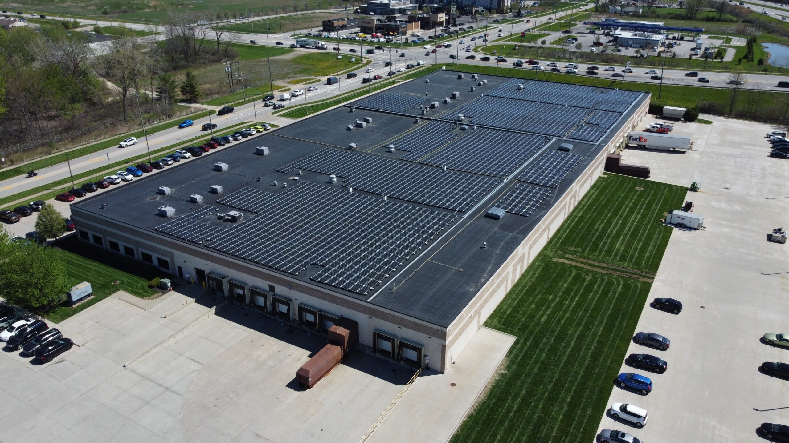 Three-quarter aerial view of the Jenne facility from the loading dock side, showing the sprawling rooftop solar panels that will offset 18,620.3 metric tons of CO₂ emissions.