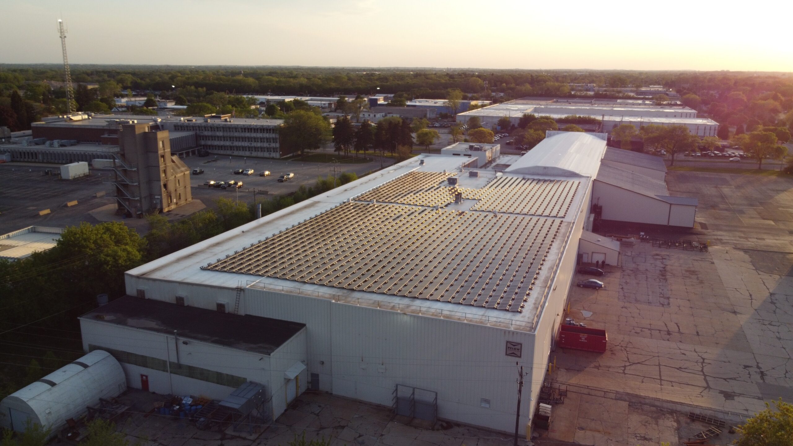 Aerial drone photograph of PFlow Industries' Milwaukee rooftop solar installation captured during golden hour, showing 1,220 panels across the facility's flat commercial roof.