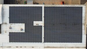 Top-down aerial drone view of the PFlow Industries rooftop solar installation in Milwaukee, showing the segmented panel layout designed around rooftop HVAC units and ventilation infrastructure, with the full 300 kW AC system visible across the flat roof membrane.